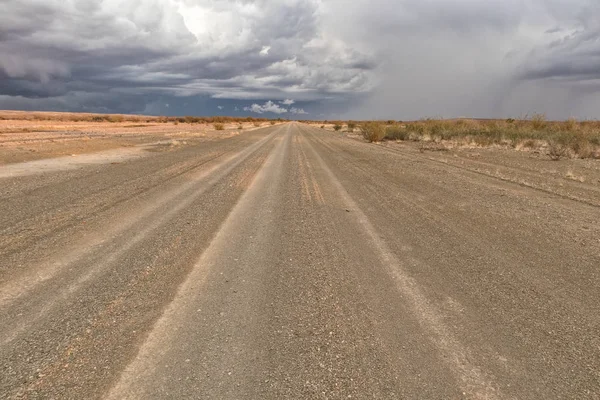 Štěrková cesta s bouřlivá obloha, po cestě do pouště Namibie. Sossuvlei. — Stock fotografie