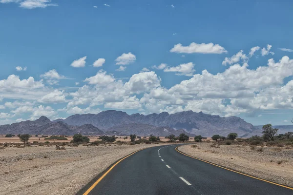 Asfaltová silnice s horami na obzoru, Namibie. — Stock fotografie