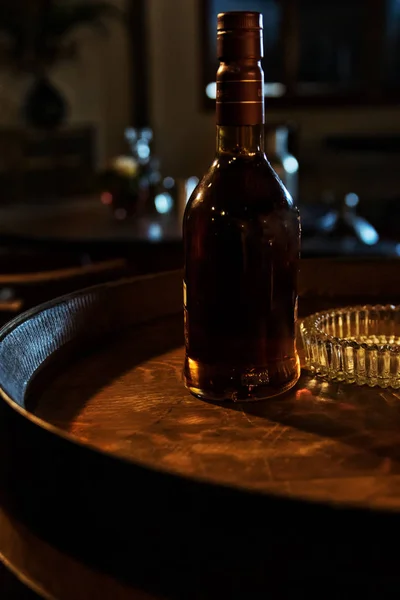 Old whiskey bottle on top of barrel, with intimate setting. — Stock Photo, Image