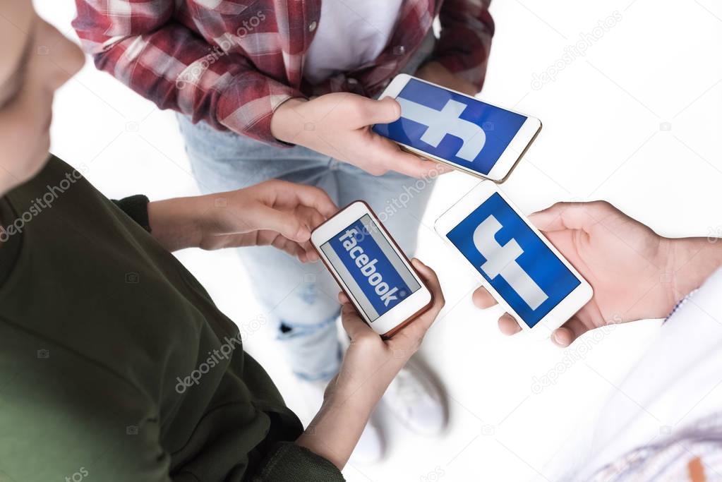 Partial view of teenage friends using smartphones with facebook logo isolated on white