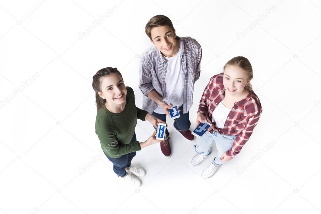 High angle view of teenage friends holding smartphones with facebook logo isolated on white