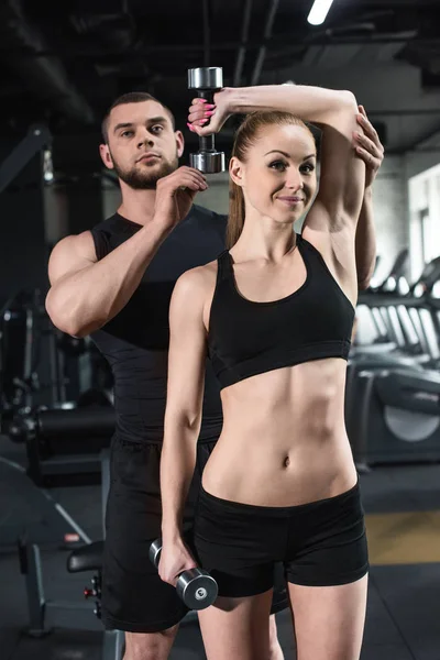 Ausbilder hilft junger Frau im Fitnessstudio — Stockfoto
