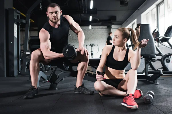 Entrenamiento del hombre mientras que la mujer sosteniendo smartphone — Foto de Stock