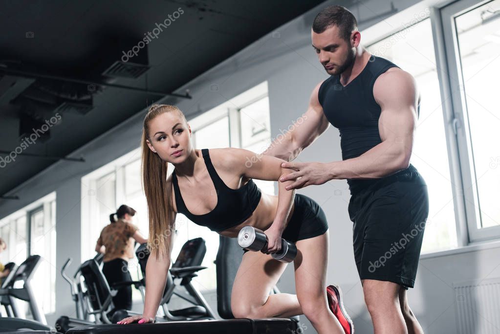 instructor helping young woman with dumbbell