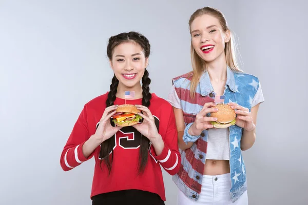 Chicas sonrientes multiétnicas sosteniendo hamburguesas — Foto de Stock