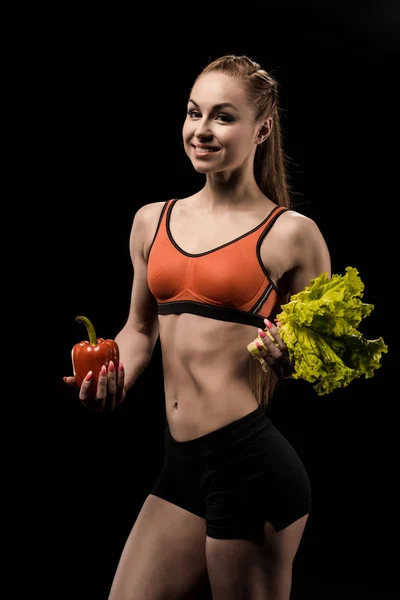 Sportswoman holding bell pepper and lettuce — Stock Photo, Image