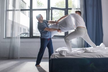 Homosexual couple fighting with pillows  clipart