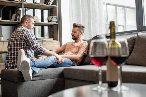 Homosexuální pár rozhovor a zároveň sedí na pohovce — Stock fotografie
