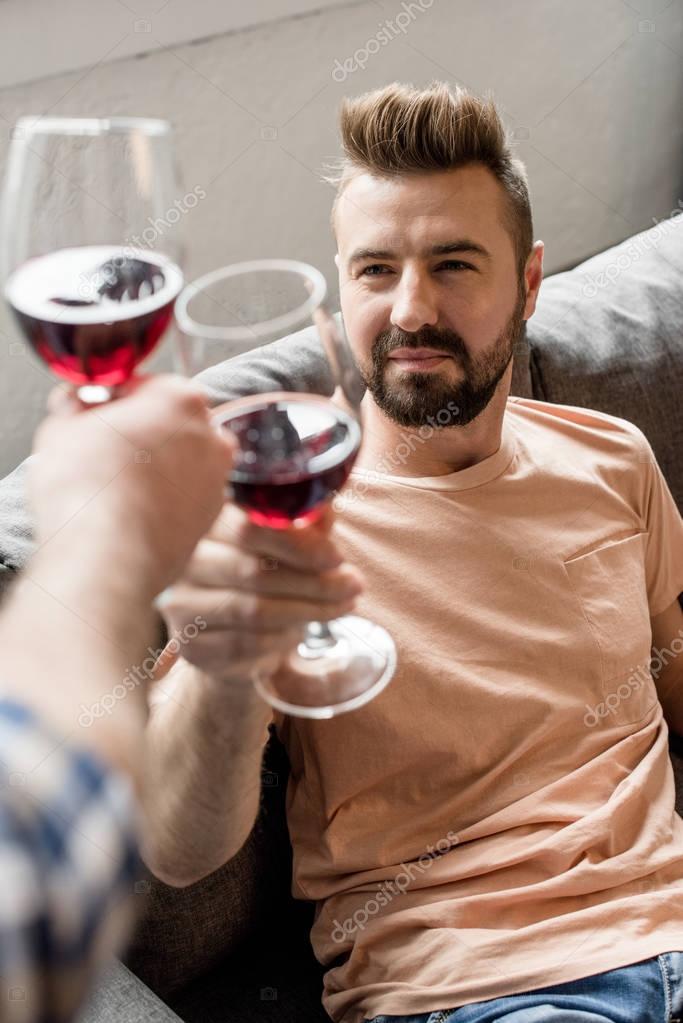 Homosexual couple clinking with wine while spending time at home