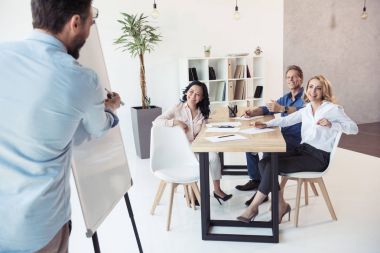 businessman writing on whiteboard while colleagues sitting clipart