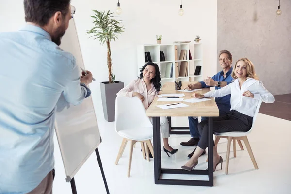 Geschäftsmann schreibt auf Whiteboard, während Kollegen sitzen — Stockfoto