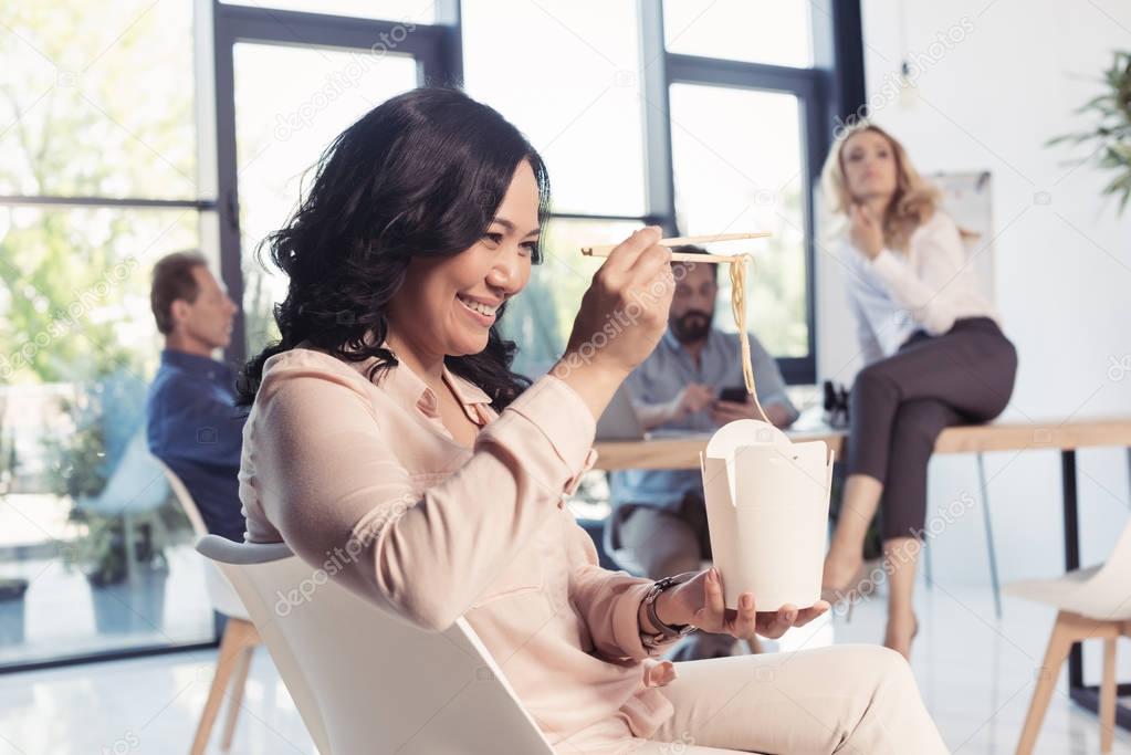 smiling asian businesswoman eating noodles