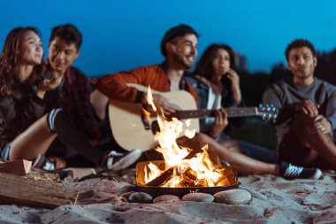 young friends spending time near campfire clipart