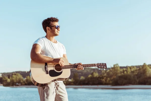 Молодой человек играет на гитаре на берегу реки — стоковое фото