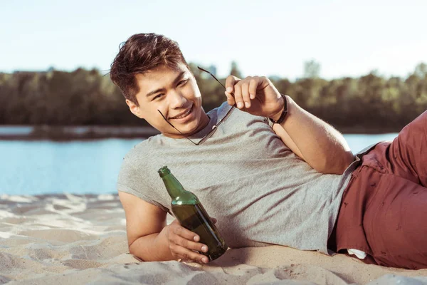 man lying on beach with bottle of beer