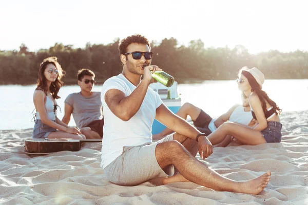 Young man drinking beer on beach — Stock Photo, Image