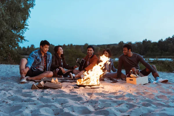Friends resting near campfire on sandy beach — Stock Photo, Image