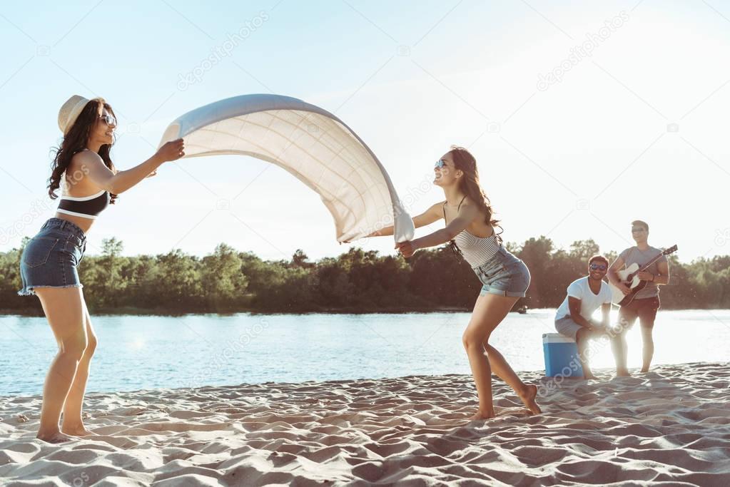 girls waving beach blanket on riverside