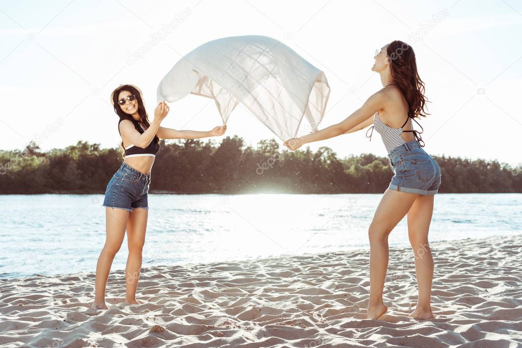 girls waving beach blanket on riverside