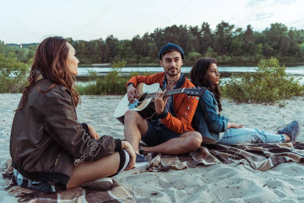 man with friends playing guitar on beach
