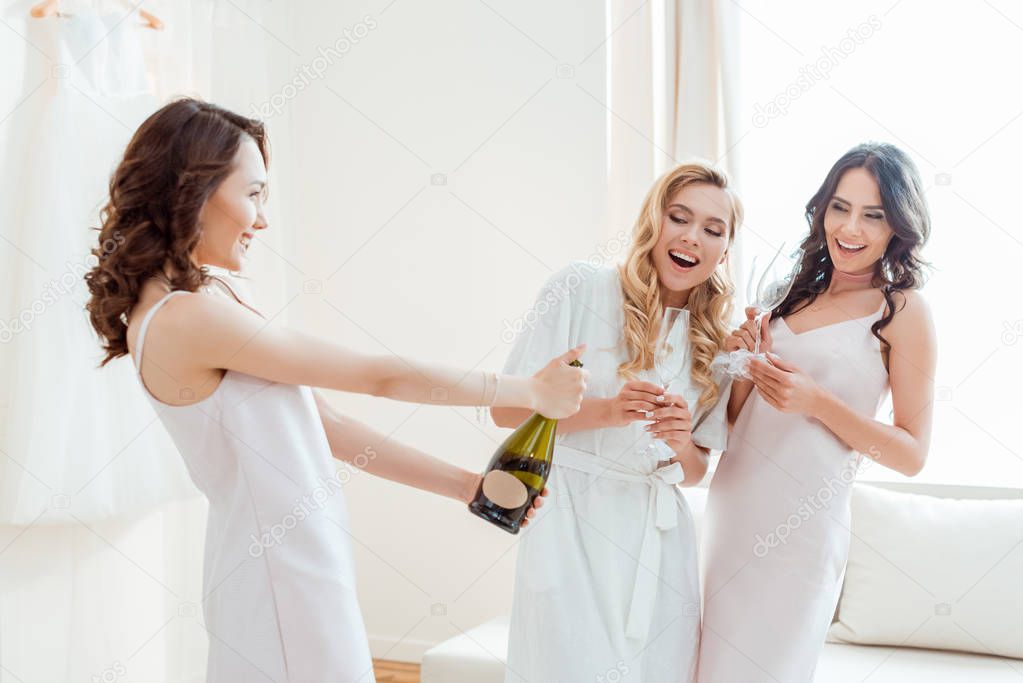 bride with bridesmaids opening champagne bottle