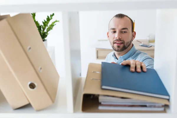 Geschäftsmann greift nach Papieren im Regal — Stockfoto