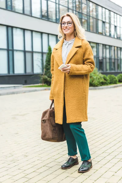 Woman in yellow coat with smartphone — Stock Photo, Image