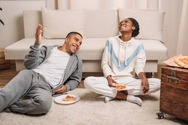 Casal comer pizza ao lado do sofá — Fotografia de Stock