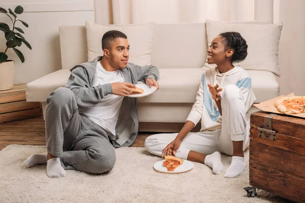 Casal comer pizza ao lado do sofá — Fotografia de Stock