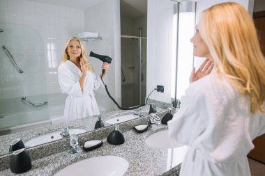 otel, banyoda saç kurutma makinesi ile saç kurutma bornoz çekici Olgun kadın