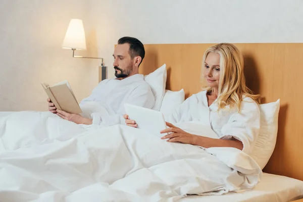 デジタル タブレットと一緒にホテルの部屋でベッドに横たわって本熟女カップル  — 無料ストックフォト