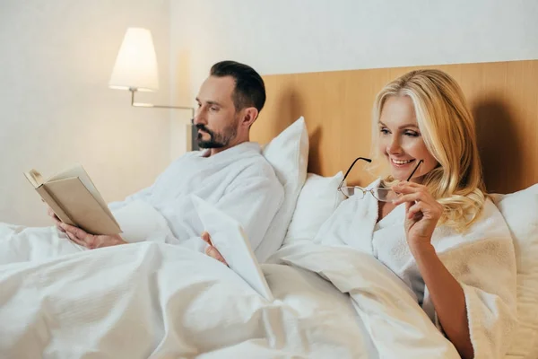 Mulher Sorrindo Segurando Óculos Usando Tablet Digital Enquanto Marido Lendo — Fotografia de Stock Grátis