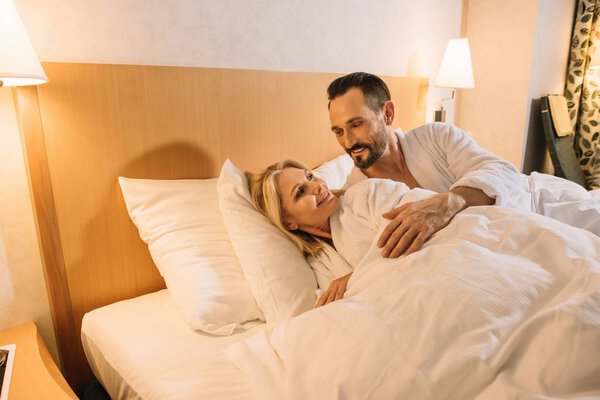 beautiful mid adult couple in bathrobes waking up in hotel room