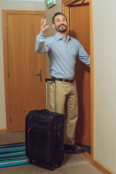 cheerful mature man with suitcase looking away while entering hotel room