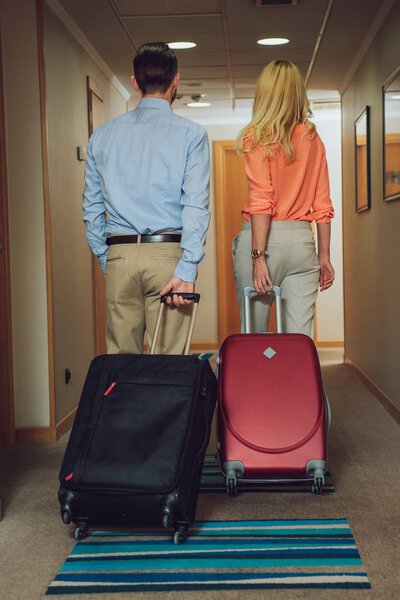 back view of middle aged couple with suitcases walking in hotel hallway