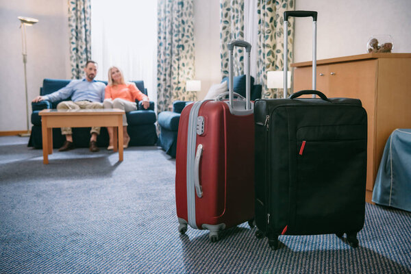 крупным планом два чемодана и зрелая пара, сидящая на диване в номере отеля
