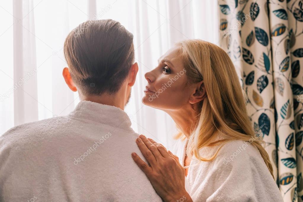 profile view of mature woman able to kiss her husband wearing bathrobe in hotel room