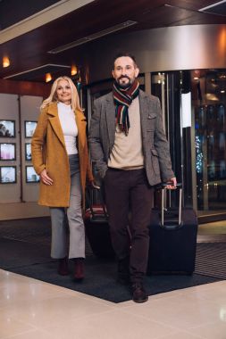 smiling mature couple with suitcases leaving hotel clipart
