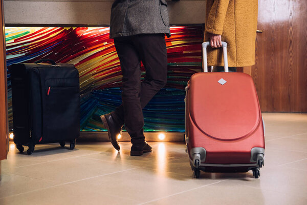 low section of mature couple with suitcases standing at reception in hotel