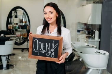 salon ayakta açık işareti ile gülümseyen esmer sahibi
