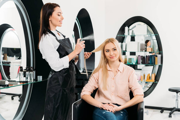 smiling hairdresser applying hair spray 