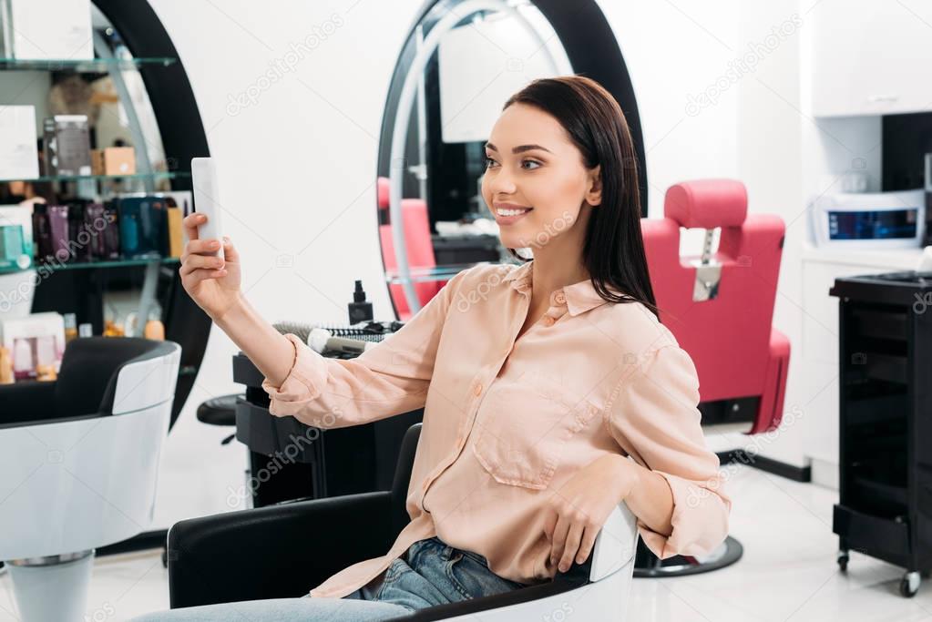 happy woman taking selfie of new hairstyle at salon