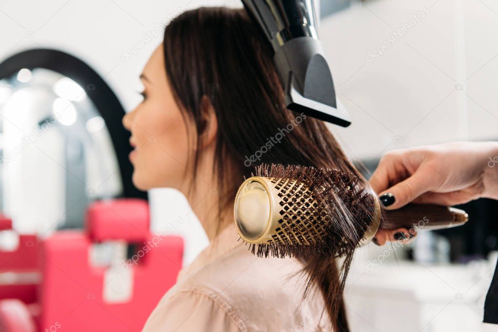 cropped image of hairdresser styling hair with round hair brush