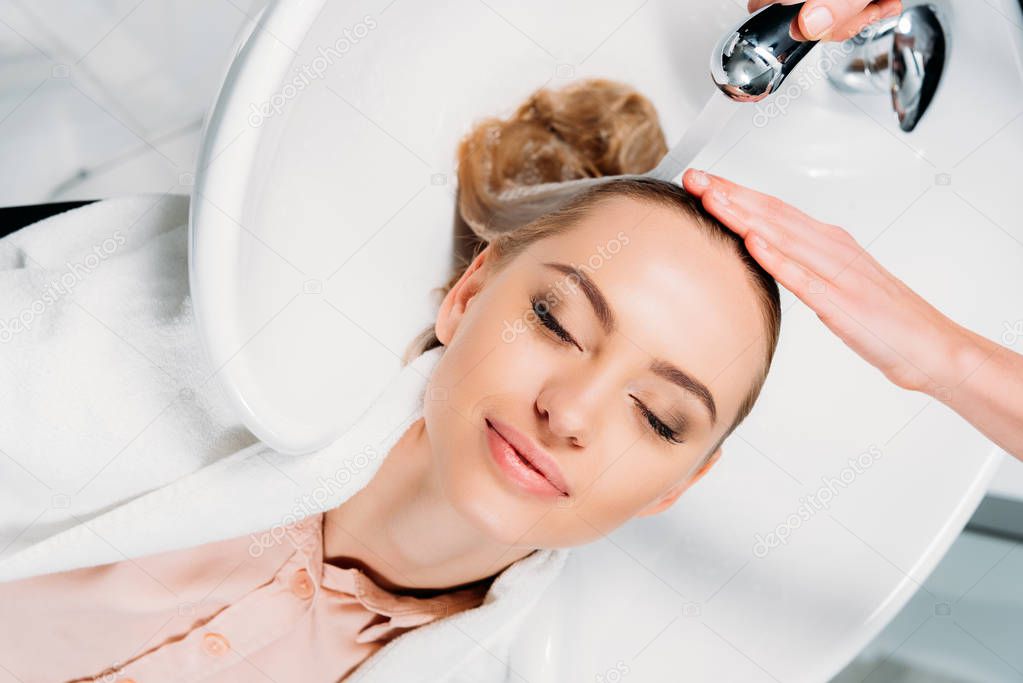 top view of customer with closed eyes lying above washbasin while hairdresser washing hair