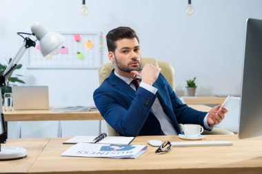 akıllı telefon tutarak ve kameraya bakarak yakışıklı işadamı