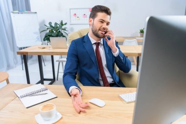 Smartphone ile konuşmak ve bilgisayar başında seyir gülümseyen iş adamı