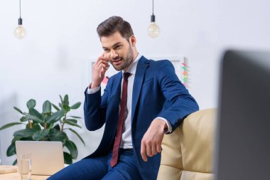 Ofiste akıllı telefonla konuşan gülümseyen işadamı.