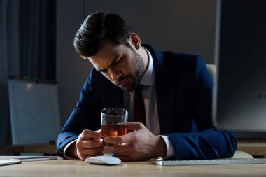 tired drunk businessman looking at glass of whiskey in office clipart