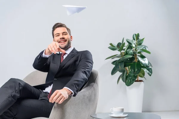 Lächelnder Geschäftsmann Sitzt Sessel Und Wirft Papierflieger Ins Büro — Stockfoto