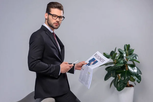 Seriös Affärsman Hålla Smartphone Och Tidningen Och Tittar Kameran — Stockfoto